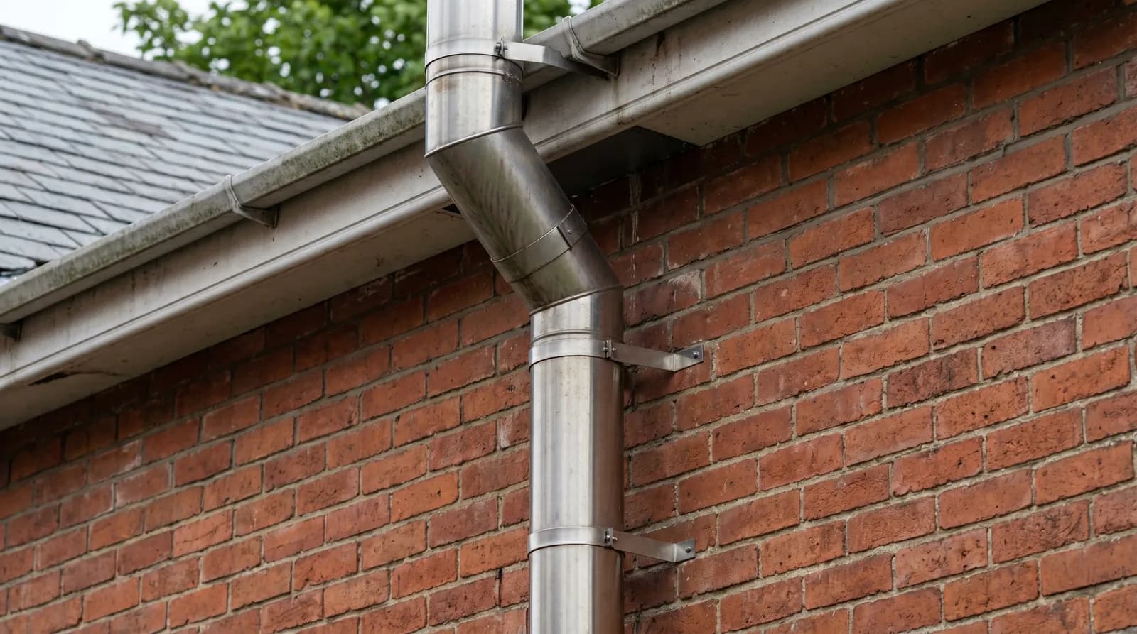 An insulated twin-wall stainless-steel flue running up the outside of a red-brick UK house wall