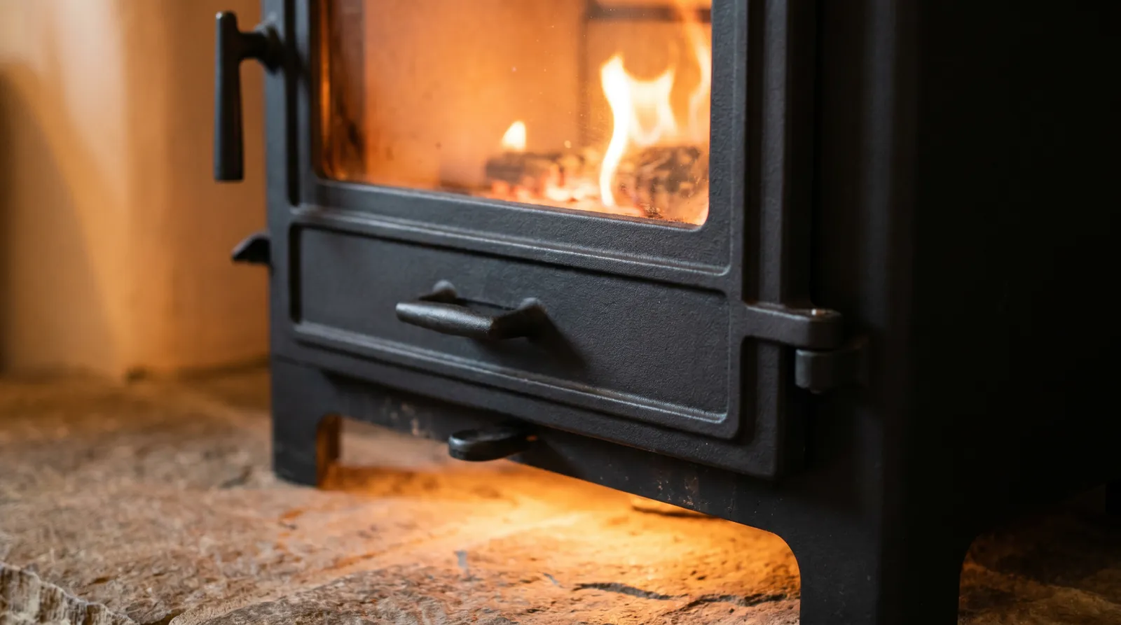 Close-up of a cast-iron stove door with a fire burning behind clean glass on a stone hearth
